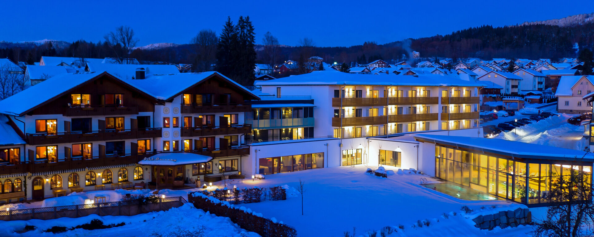 Das winterlich eingeschneite Hotel Eibl-Brunner in Frauenau. Alle Fenster sind beleuchtet und die Umgebung ist ebenfalls mit Schnee bedeckt.