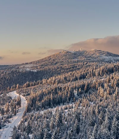 Eibl Brunner: dein Hotel in Frauenau Verschneite Tannen und ein verschlungener Weg im winterlichen Gebirge bei Sonnenuntergang