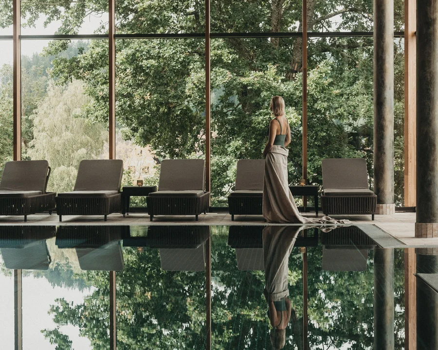 Eibl Brunner: dein Hotel in Frauenau Frau steht neben Pool mit Blick auf große Fenster und grüne Bäume