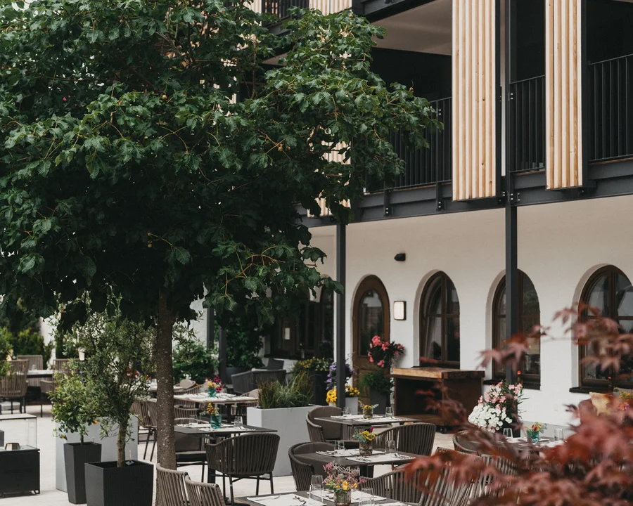 Eibl Brunner: dein Hotel in Frauenau Außenbereich eines Restaurants mit Tischen, Stühlen und Bäumen vor einem modernen Gebäude