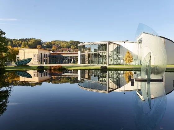 Eibl Brunner: dein Hotel in Frauenau Modernes Gebäude mit Glasfassade und Skulptur am ruhigen Teich